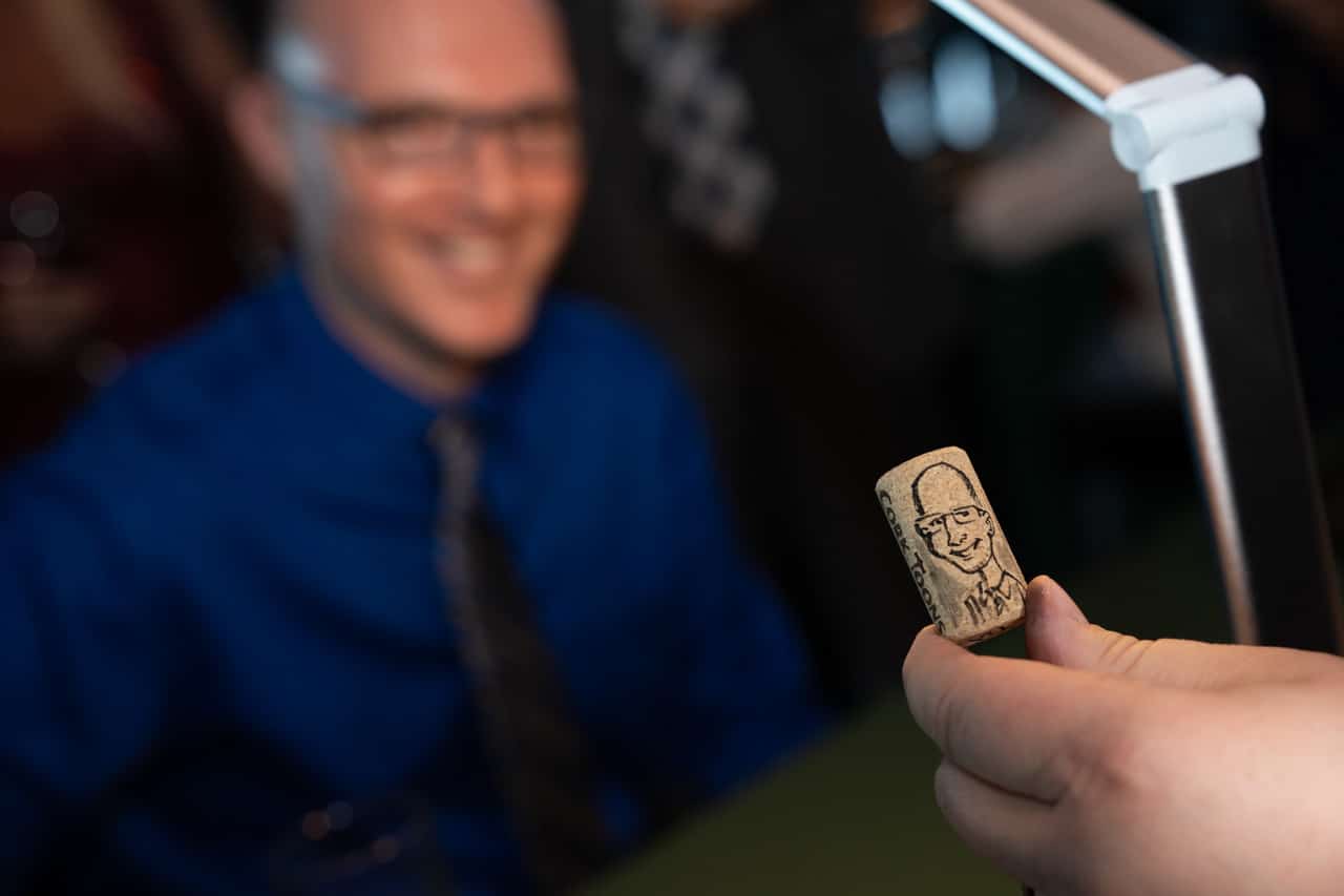 A sketch of a man drawn on a wine cork while he looks on smiling