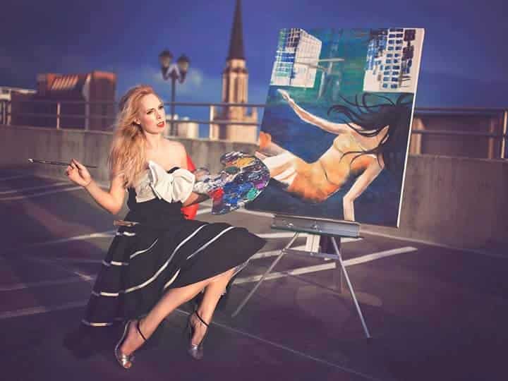artist posing while she paints a woman on a rooftop