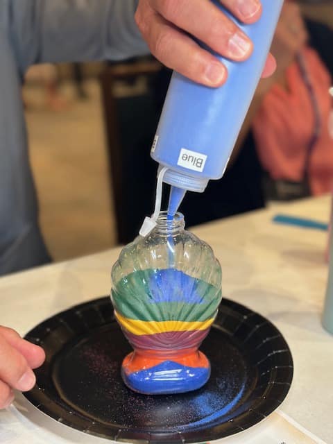 person pouring blue sand into seashell shaped glass bottle